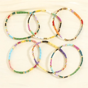 Close-up of six colorful Tila bead bracelets with gold accents on beige silk fabric