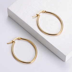 Elegant gold oval hoop earrings in polished titanium steel on a minimalist white display