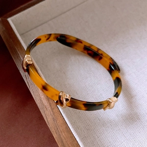 Detail of leopard print resin bangle with gold buckle on elegant wooden tray display