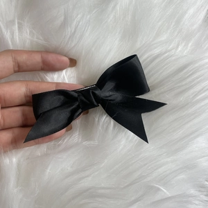 Handheld view of a large black satin bow hair clip on a soft white plush background