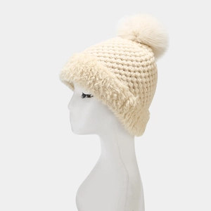 Detail of cream white cable knit hat with thick faux fur lining and large fluffy pom-poms