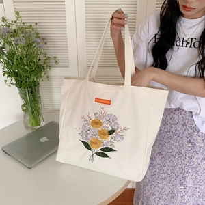 Detail shot of embroidered daisy flowers on a cream canvas tote bag with a solarra tag