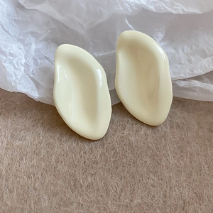 Dettaglio di orecchini a goccia color crema su uno sfondo di feltro beige morbido