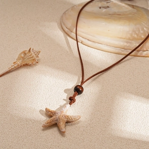 Collier pendentif étoile de mer avec cordon marron et perle bois sur fond de sable