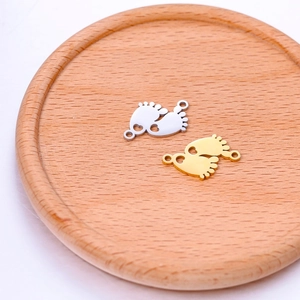 Macro detail of gold and silver baby feet pendants with heart cutouts on a wooden tray