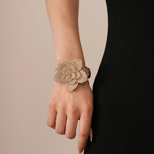 Detailed close-up of a large gold flower bangle with rhinestones on a woman's wrist