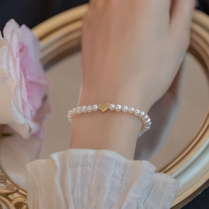 Elegant freshwater pearl bracelet with a gold heart charm worn on a wrist