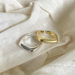 Close-up of minimalist square rings in gold and silver on soft linen fabric