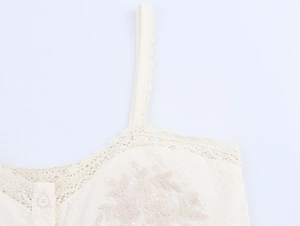 Gros plan sur un caraco blanc crème avec des bordures en dentelle et broderie florale
