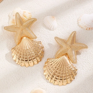 Detail shot of golden starfish and seashell earrings resting on white sand beach background