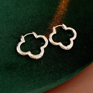 Macro shot of silver hollow clover hoop earrings resting on dark green velvet padding