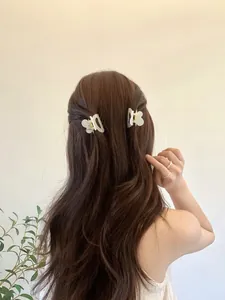 Détail de deux pinces à cheveux papillon blanches mates sur des cheveux bruns ondulés