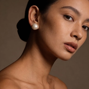 Close-up of a large white pearl stud earring worn by a model in a minimalist style