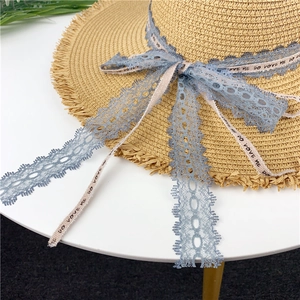 Close-up of straw sun hat featuring frayed edges and blue lace ribbon with text detail