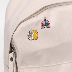 Creative enamel pins with brain flowers and pink lungs attached to a canvas backpack