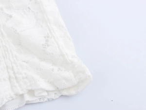 Close-up of intricate white floral lace texture and stitching details on the mini dress