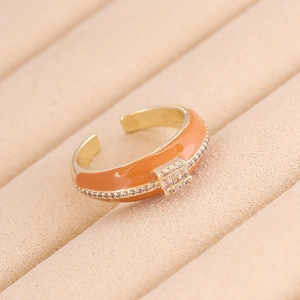 Dettaglio dell'anello dorato in smalto arancione con zirconi su vassoio in velluto