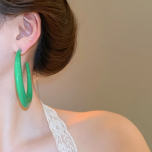 Close-up of a model wearing large glossy green geometric C-shaped hoop earrings