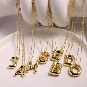 Close-up of golden puffy alphabet pendant necklaces A B D E J M O S on white display