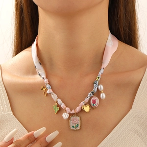 Detail view of pink floral fabric chain necklace with gold charms and pearls on model neck
