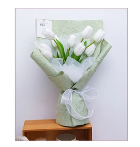 Detail of faux white tulips wrapped in textured light green paper with white ribbon