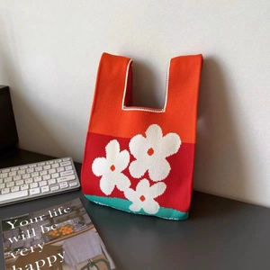 Primo piano di una borsa in maglia tricolore con motivi a fiori bianchi su un tavolo