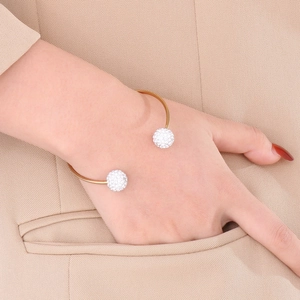 Detailed shot of a gold C-shaped titanium bracelet with crystal-studded balls on a blazer
