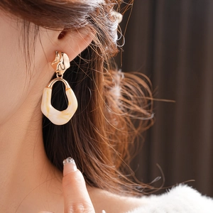Close-up of model wearing oval resin earrings with cream marble pattern and gold studs