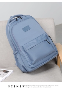 Close-up of a blue nylon backpack with side pocket and handle on a grey fabric chair