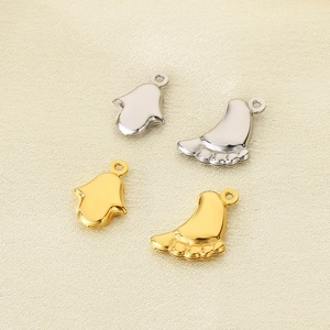 Detailed macro view of gold and silver stainless steel hand and foot pendants on beige fabric