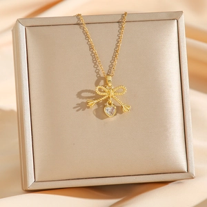 Elegant gold bow necklace with heart-shaped zircon pendant on champagne silk background