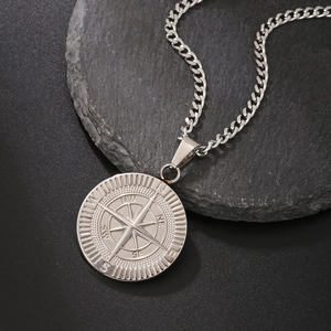 Macro detail of silver compass pendant with N/S/E/W engraving and chunky cuban chain