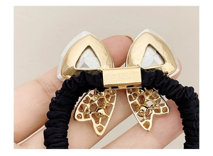 Close-up of black scrunchie with golden bow charm and white faceted stones inlay