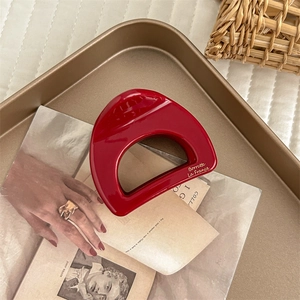 Detail of a red D-shaped hair claw clip on a golden tray with a vintage aesthetic