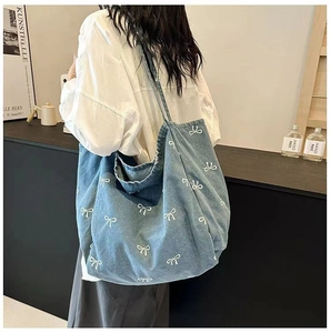 Detailed back view of a blue denim tote bag with white bow embroidery on a female model