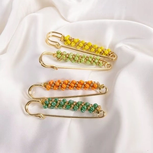 Detailed view of four colorful beaded safety pin brooches on white satin fabric