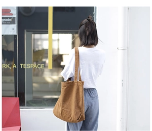 Close-up of a brown canvas tote bag worn over the shoulder in a stylish urban setting