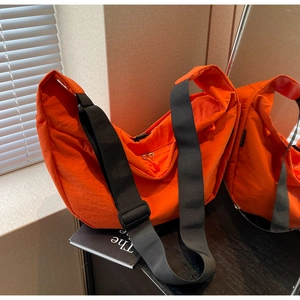 Detail view of the large orange nylon dumpling bag with adjustable wide strap and zip closure