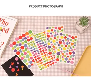 DIY colorful stickers in star, heart, and circle shapes with pink tweezers on plaid background