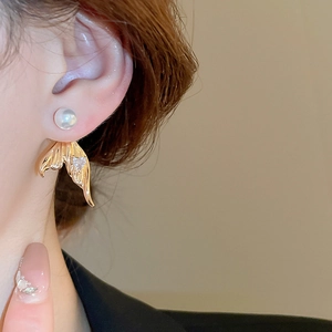 Macro detail of mermaid tail earring with golden metal, white pearl and zircon heart