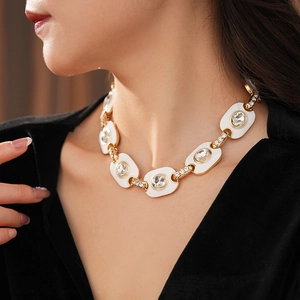 Gros plan d'un collier vintage doré avec maillons blancs et cristaux sur le cou