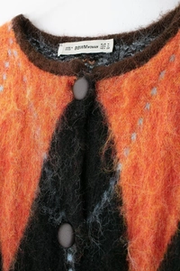 Détail du cardigan en maille losange orange et noir avec texture mohair pelucheuse