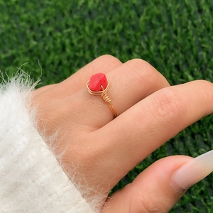 Detail of a handmade gold wire-wrapped ring with a vibrant red stone on a finger