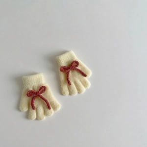 Flat lay of cream yellow knitted gloves with red bow details on a white background