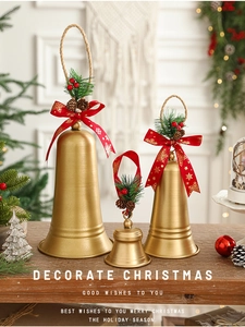 Close-up of golden Christmas bells with red snowflake ribbons and green pine needles decoration