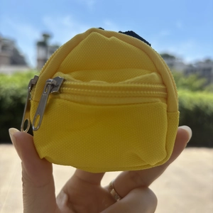 Close-up of a mini yellow canvas backpack keychain with double silver zippers in hand