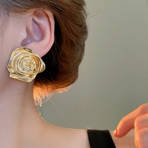 Orecchino a perno a forma di rosa dorata con petali in metallo su modella in primo piano