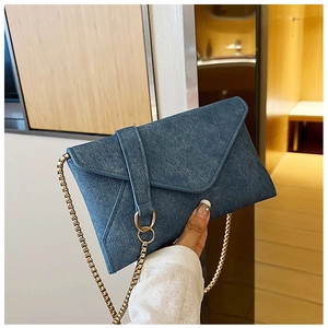 Detailed close-up of blue denim envelope bag with golden chain strap and woven texture