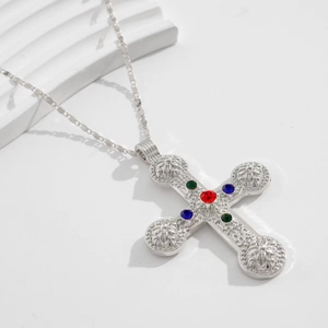 Détail d'un pendentif croix argenté avec des pierres précieuses rouges, bleues et vertes