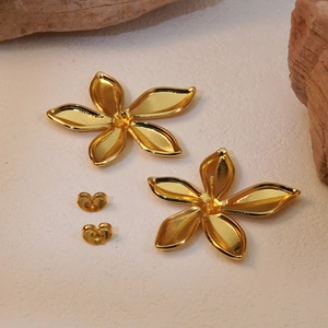 Macro shot of gold five-petal flower earrings with butterfly backs on a stone surface